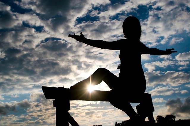 Femme pratiquant le yoga, sport bien-être, sur fond de ciel ponctué de nuages.