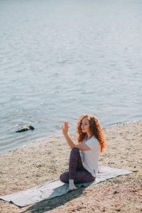 Un femme réalise un exercice de yoga sur son tapis au bord de l'eau.