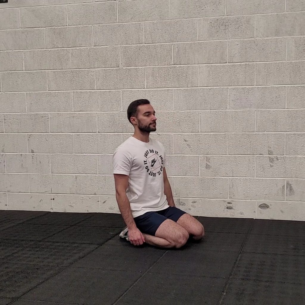 Position de départ du kneeling jump squat, à genou dans une salle dédiée au sport.