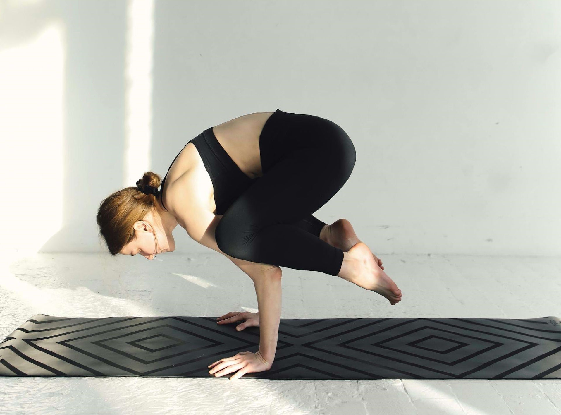 Une femme réalise la posture du corbeau sur un tapis de yoga.