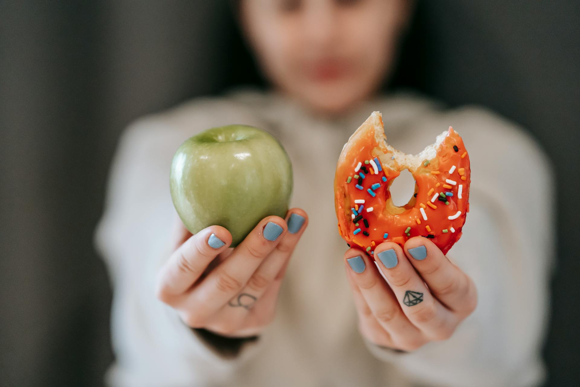 Une personne montre une pomme et un donuts pour comparer leurs valeurs nutritionnelles.