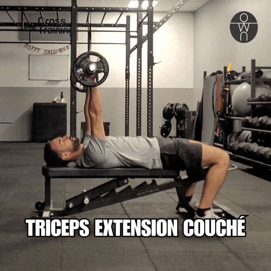 Gif de notre coach sportif dans sa home gym, en train de réaliser les triceps extensions couché à la barre, sur un banc de musculation.