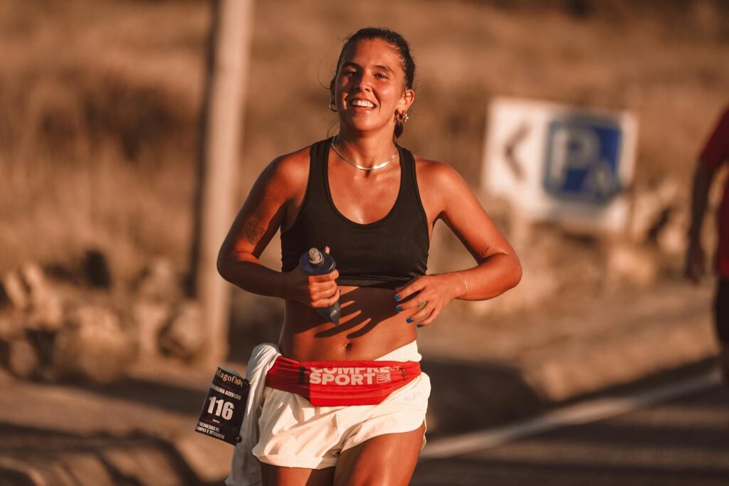 Une femme porte un numéro de course en pleine compétition, une gourde à la main.