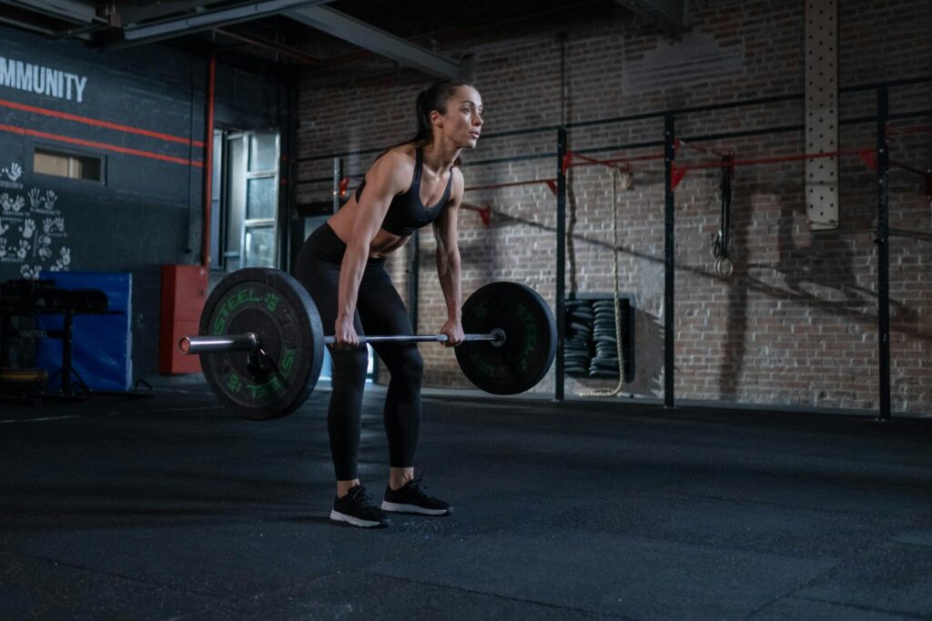 Une femme soulève une barre lestée dans une salle de sport et en tenue de sport.