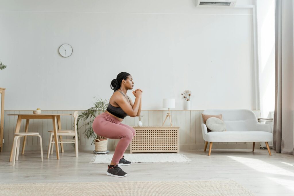Une femme en tenue de sport dans son salon réalise un exercice pour quadriceps très connu : le squat !