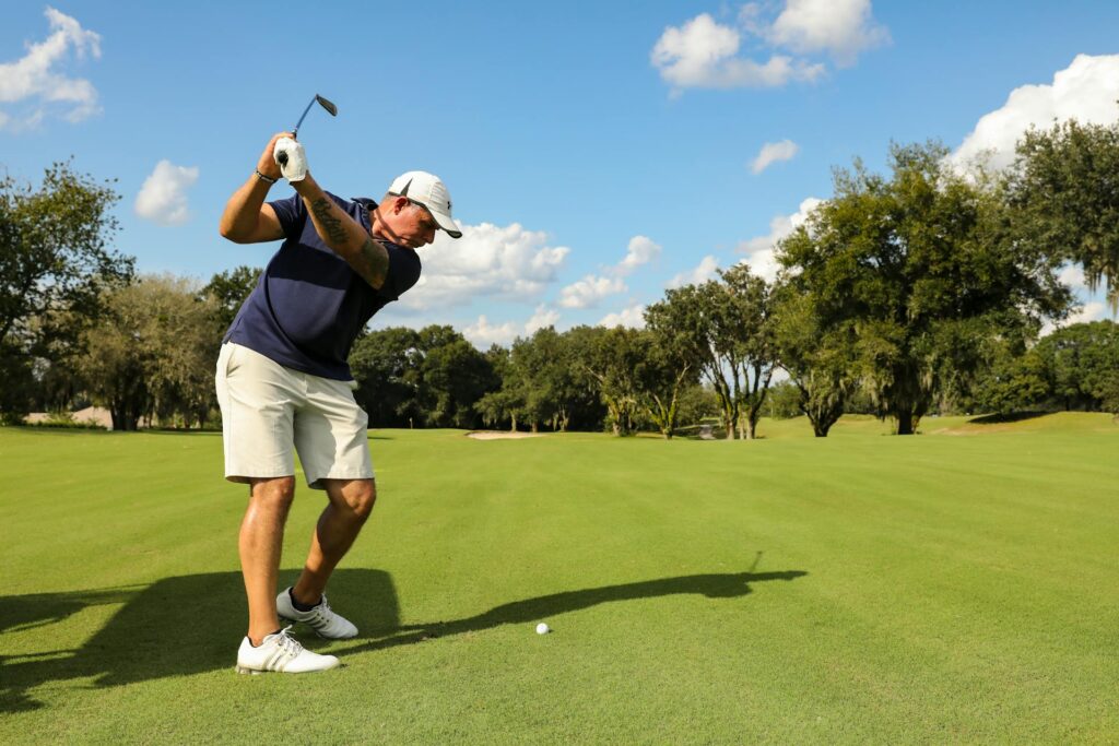 Un golfeur lève son club, sur le point de frapper une balle de golf au sol.