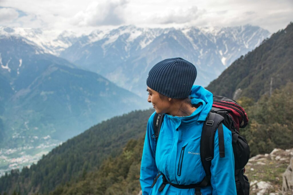 Au milieu des paysages de montagne, une femme en tenue d'hiver portant un bonnet et un sac de randonnée.