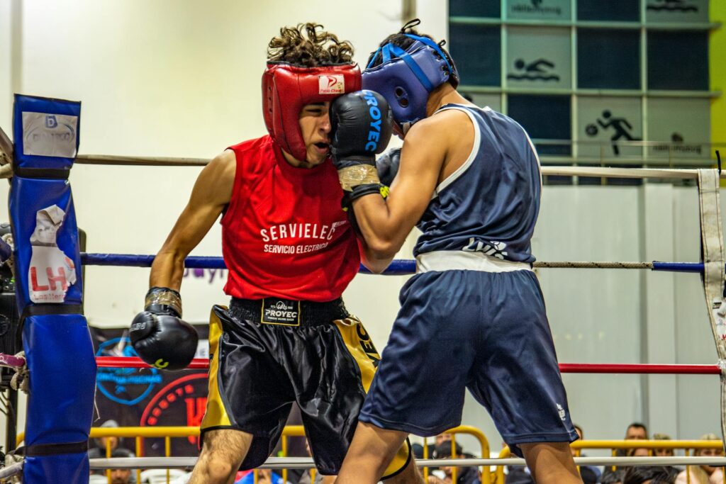 Deux boxeurs s'affrontent sur le ring, dans leur tenue de boxe et avec leur casque de protection et leurs gants.