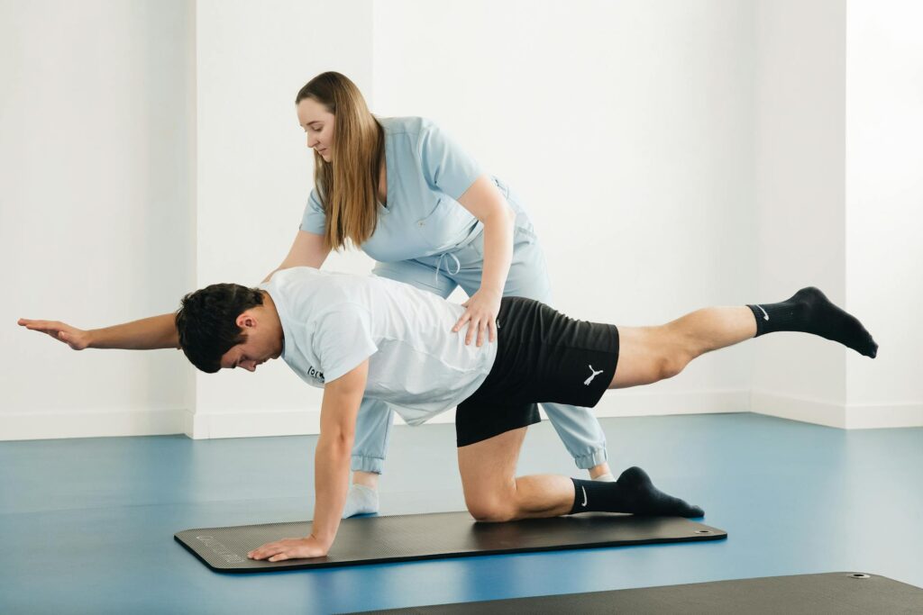 Une coach en réathlétisation aide un homme sportif à faire du gainage pour récupérer d'une fracture de fatigue.