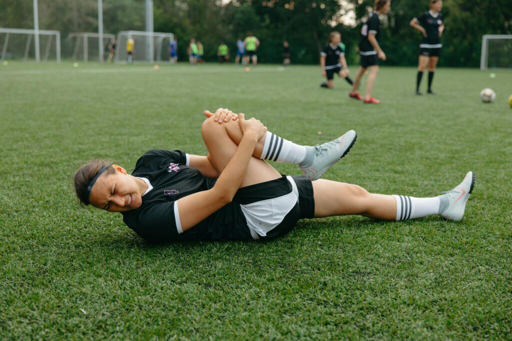 Une joueuse de foot allongée sur le terrain se tient le bas de la jambe en grimançant.