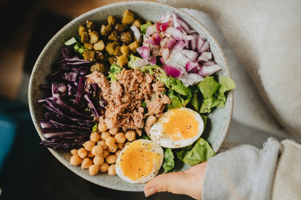 Une assiette avec des cornichons, du chou rouge, des pois chiches, des œufs, du thon, de la salade et des oignons rouges.