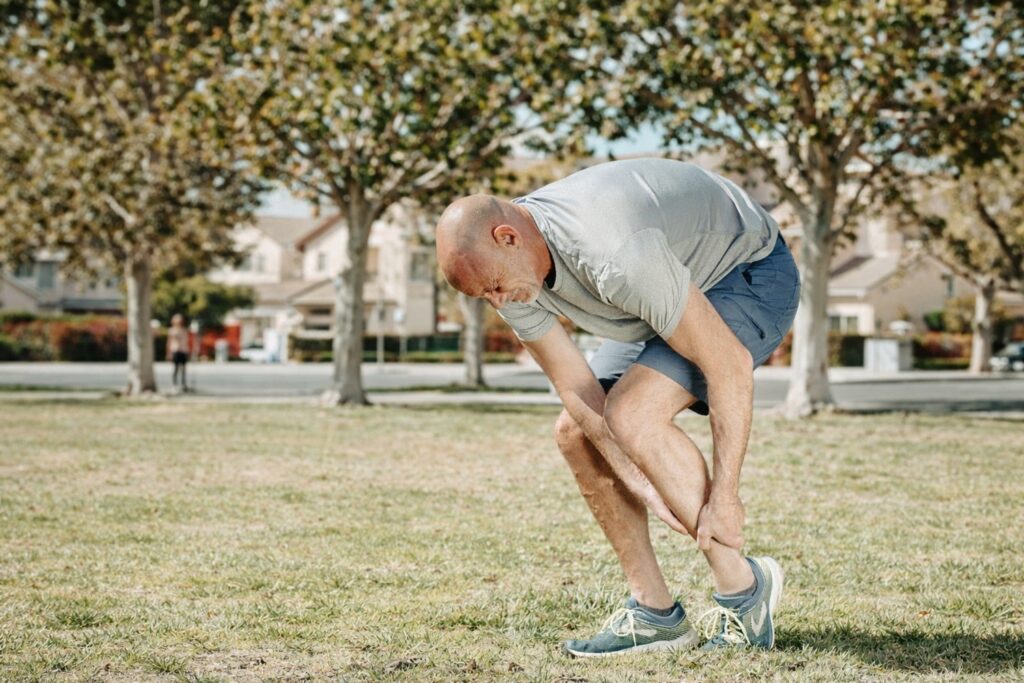 Un homme en tenue de sport se tient la cheville avec une expression de douleur.