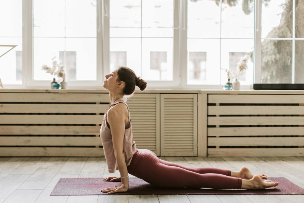 Une femme en tenue de pilates, en posture de départ du swan dive, sur un tapis dans son appartement.